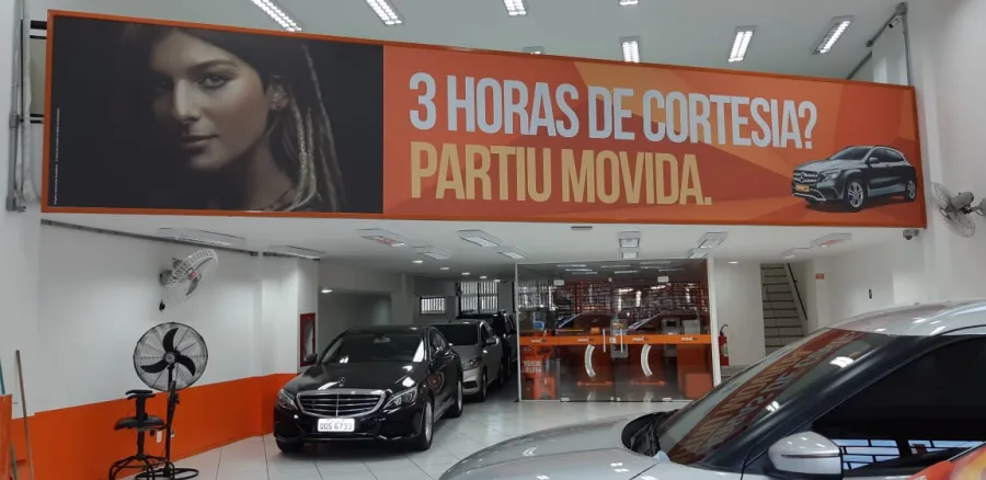 Banner promocional impresso em grande formato instalado em loja Movida — impressão látex da Do it! Print, Rio de Janeiro